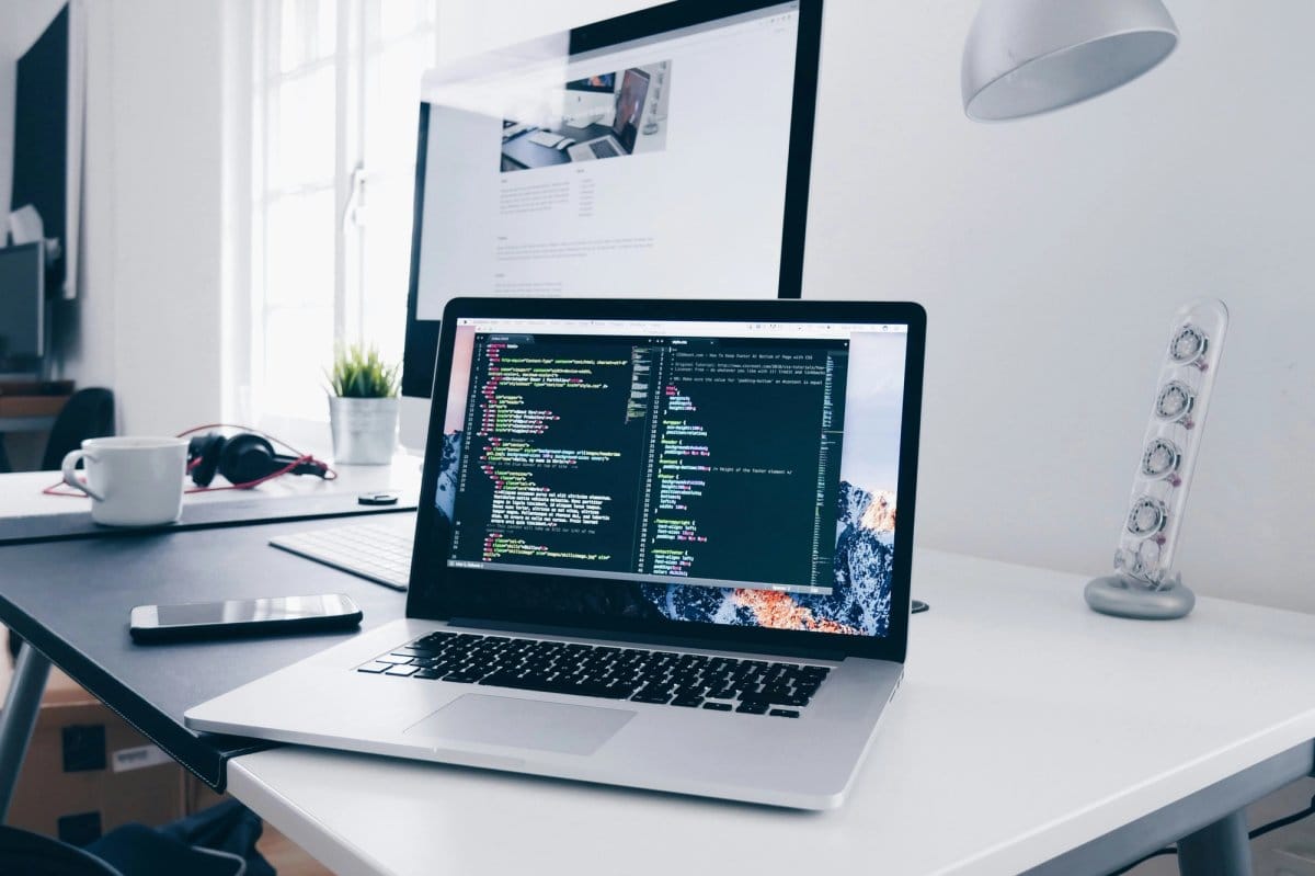 Laptop met code op een bureau, met een monitor en bureaulamp